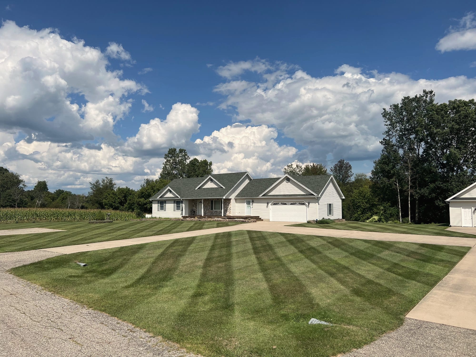 A striped lawn along a curved driveway leading to a white house