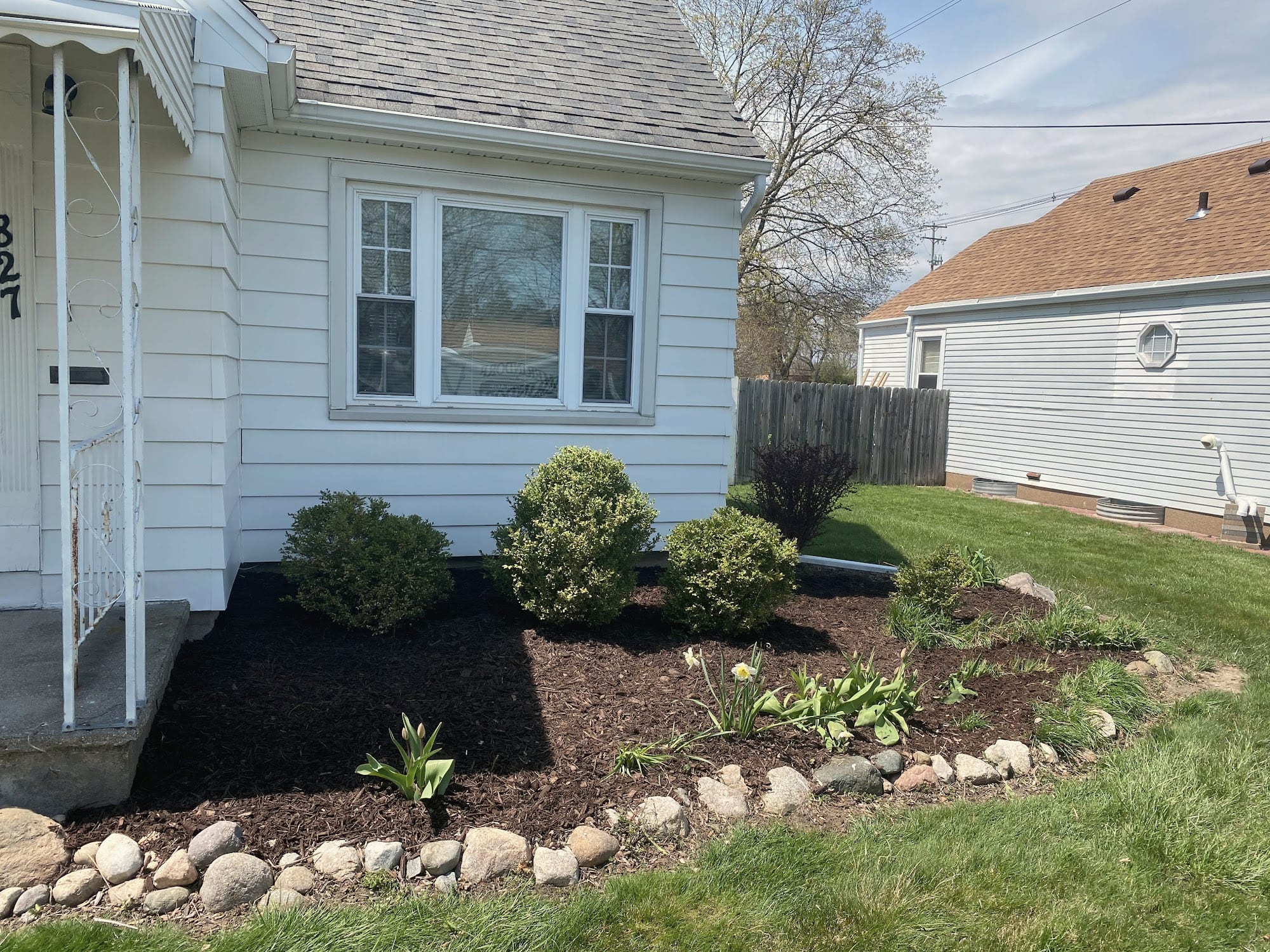 A fresh bed of dark mulch with shrubs and a stone border beside a white house